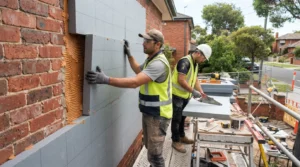Professional installers fitting exterior insulation panels before rendering a Melbourne home.